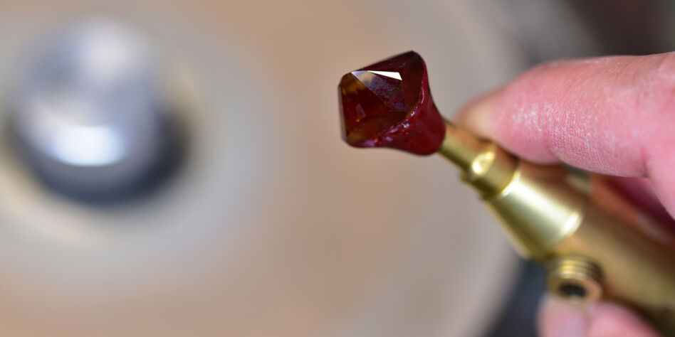 Craftsman's hand holding metal dop with citrine stone during faceting process.