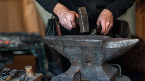 Blacksmith at the workshop. Working metal with hammer and tools on the anvil in the forge.
