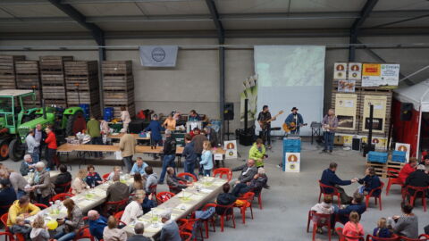 Witloofteelt Open Bedrijvendag. Geïntresseerden verzamelen zich in een hangar en luisteren naar een muziekband.